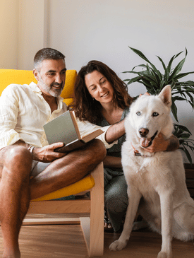 a man sitting on a chair with a women sitting next to him hugging a big white dog